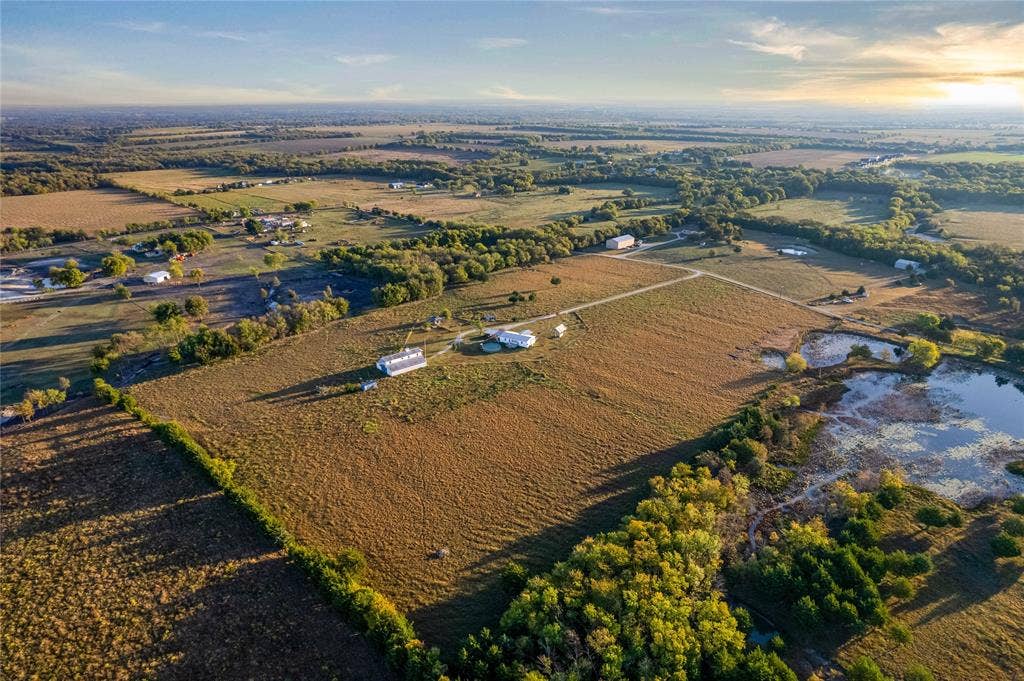1154 Outlaw Trail, Wolfe City, TX 75496 Aerial perspective of expansive acreage featuring open pasture, mature trees, a private pond, and multiple structural improvements