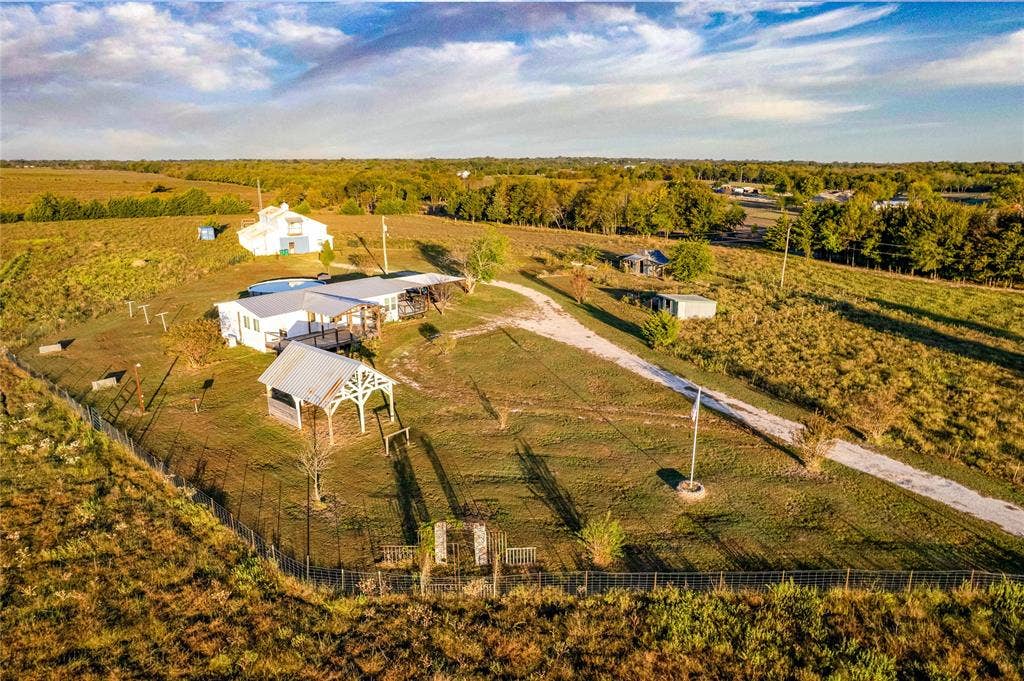 1154 Outlaw Trail, Wolfe City, TX 75496 Expansive acreage featuring a gated perimeter, gravel driveway, detached metal pavilion, and multiple outbuildings