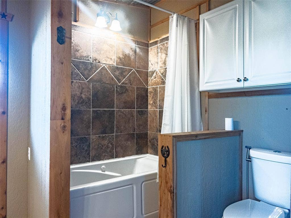 1154 Outlaw Trail, Wolfe City, TX 75496 Bathtub surround with neutral-toned square tile, white wall-mounted cabinetry, integrated light fixture, and wood-trimmed partition wall