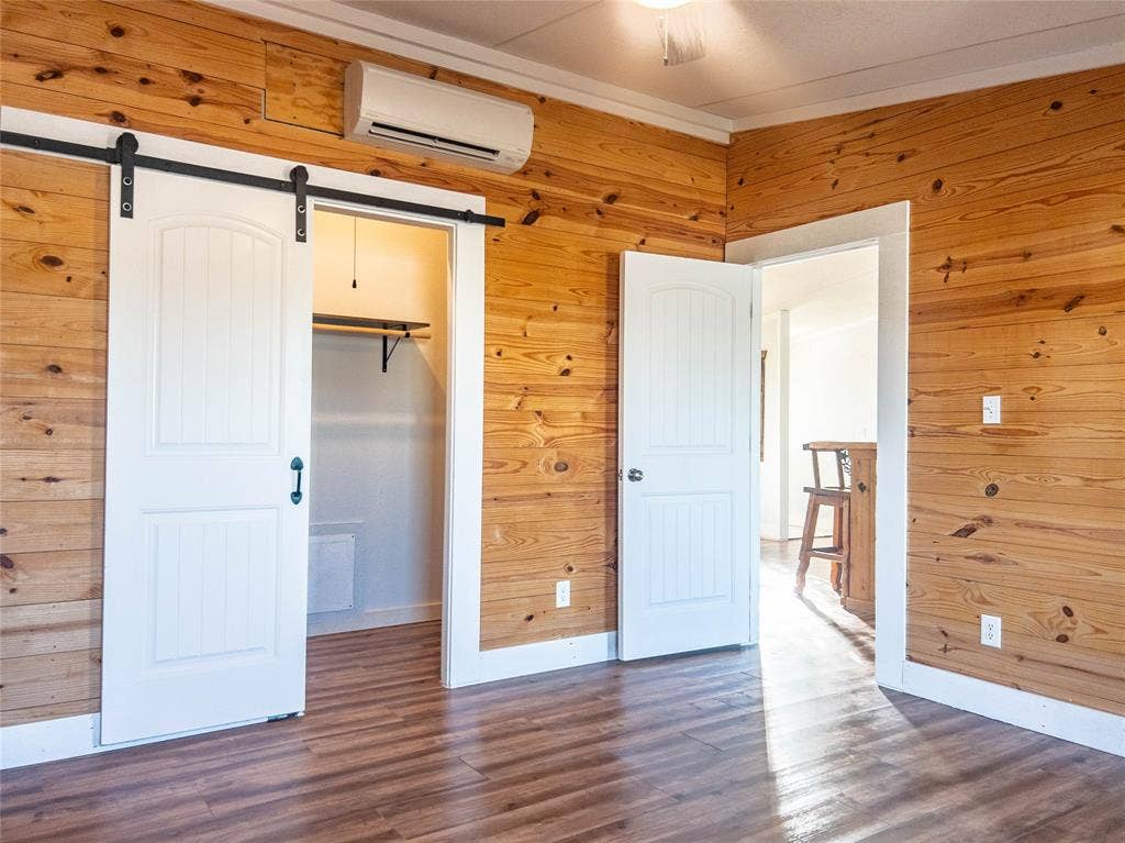 1154 Outlaw Trail, Wolfe City, TX 75496 Interior featuring horizontal wood wall paneling, wood-finish flooring, a sliding white barn door, and a wall-mounted climate control unit
