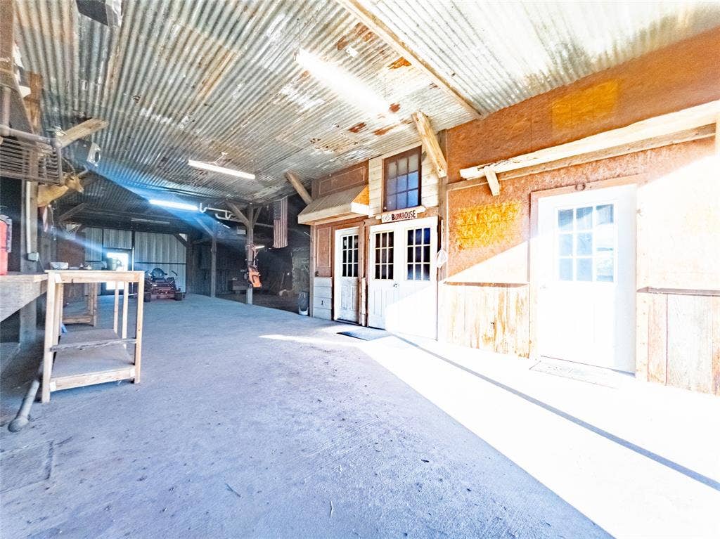 1154 Outlaw Trail, Wolfe City, TX 75496 Interior workspace featuring a corrugated metal ceiling, exposed structural timber beams, concrete flooring, and multiple exterior-style entry doors