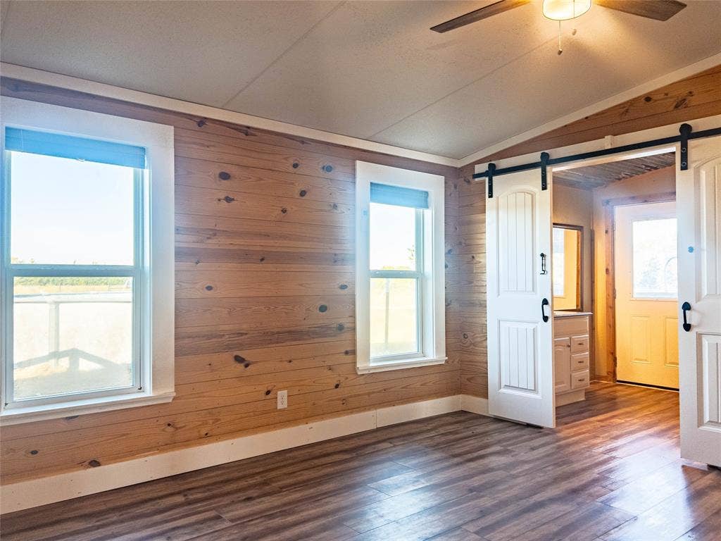 1154 Outlaw Trail, Wolfe City, TX 75496 Interior featuring knotty pine wall paneling, wood-finish flooring, two sliding barn-style doors, and a ceiling fan with light fixture