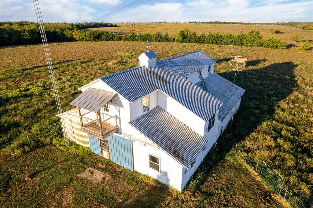1154 Outlaw Trail, Wolfe City, TX 75496 Aerial view of a structure featuring a metal roof, a cupola, a second-story wooden balcony, and white siding, set on an expansive parcel of land