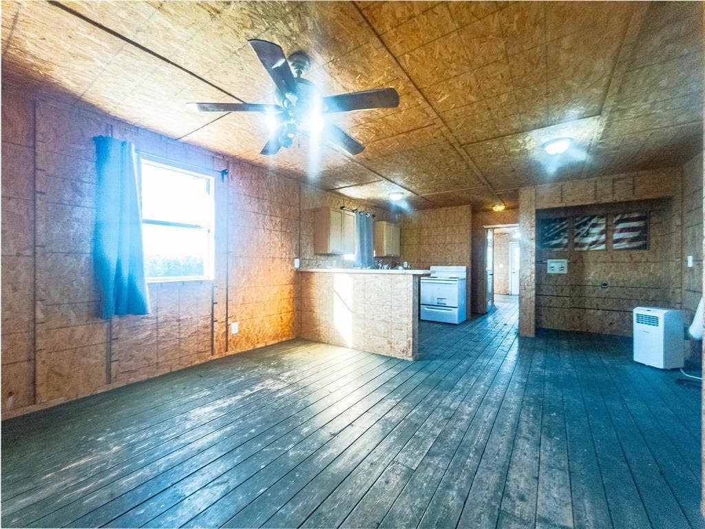 1154 Outlaw Trail, Wolfe City, TX 75496 Open-concept interior featuring oriented strand board walls and ceiling, painted wood-plank flooring, a kitchen breakfast bar, and a ceiling fan with integrated lighting