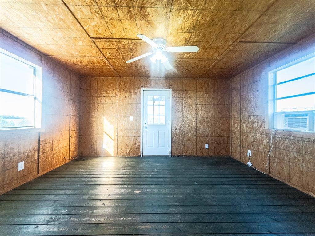 1154 Outlaw Trail, Wolfe City, TX 75496 Interior room featuring oriented strand board wall and ceiling paneling, painted wood-plank flooring, dual windows, a central ceiling fan with integrated lighting, and a multi-pane exterior door