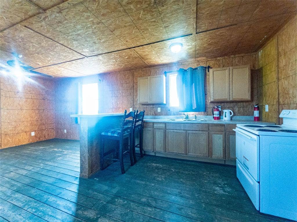 1154 Outlaw Trail, Wolfe City, TX 75496 Oriented strand board (OSB) interior walls and ceiling, wood-plank flooring, cabinetry with bar-style counter, and integrated electric range