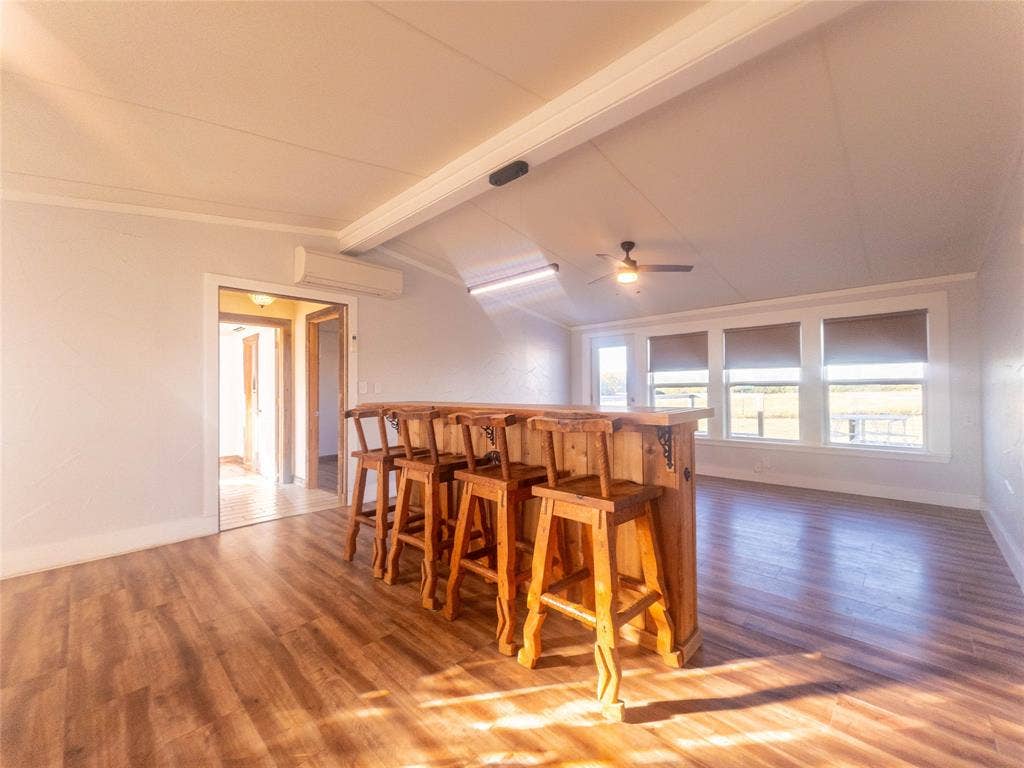 1154 Outlaw Trail, Wolfe City, TX 75496 Interior space featuring wood-finish flooring, vaulted ceilings, a built-in wood bar, a ceiling fan, and large windows with integrated blinds
