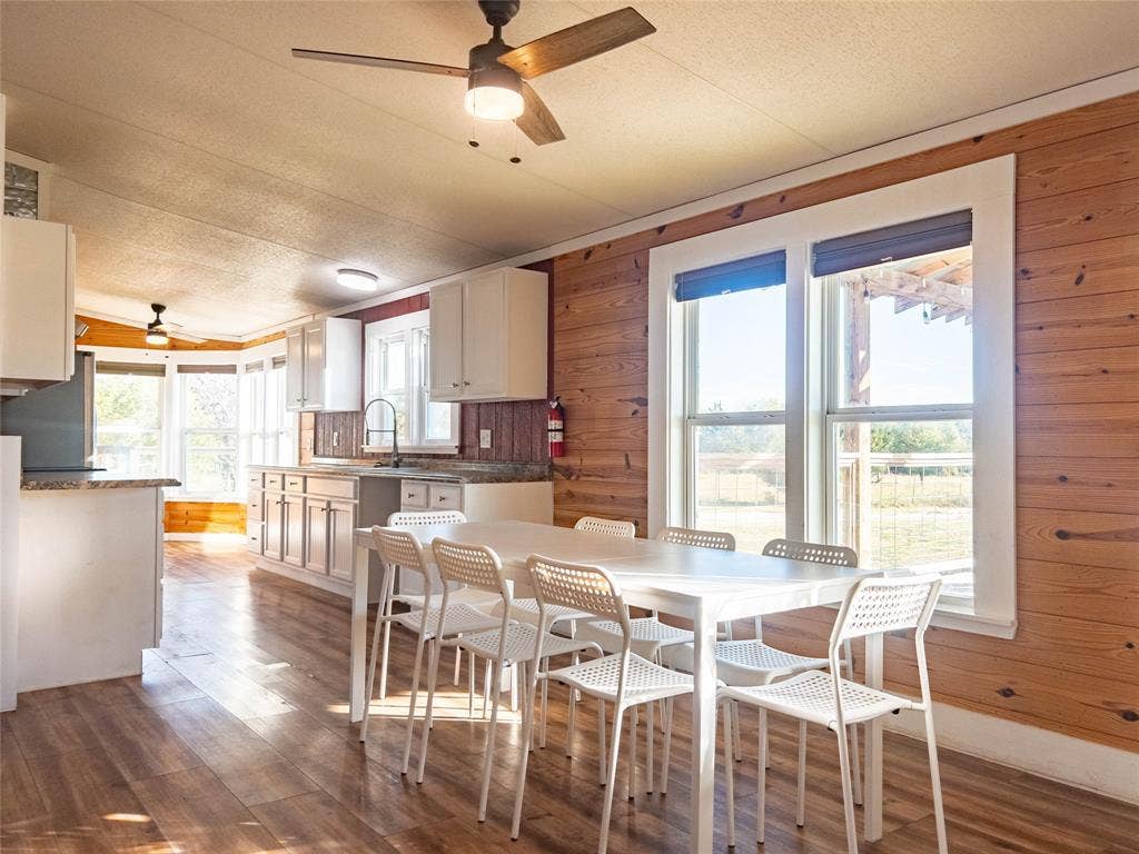 1154 Outlaw Trail, Wolfe City, TX 75496 Kitchen featuring horizontal wood-paneled walls, wood-finish flooring, white cabinetry, solid-surface countertops, and a ceiling fan with integrated lighting