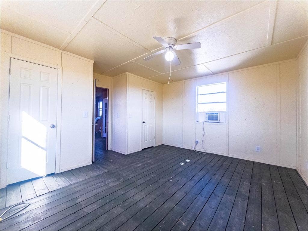 1154 Outlaw Trail, Wolfe City, TX 75496 Interior space featuring dark-finish plank flooring, paneled walls, a ceiling fan with integrated lighting, and two interior doors
