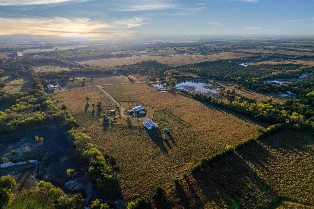 1154 Outlaw Trail, Wolfe City, TX 75496 Aerial perspective of expansive acreage featuring open pasture land, established tree lines, multiple outbuildings, and a private pond
