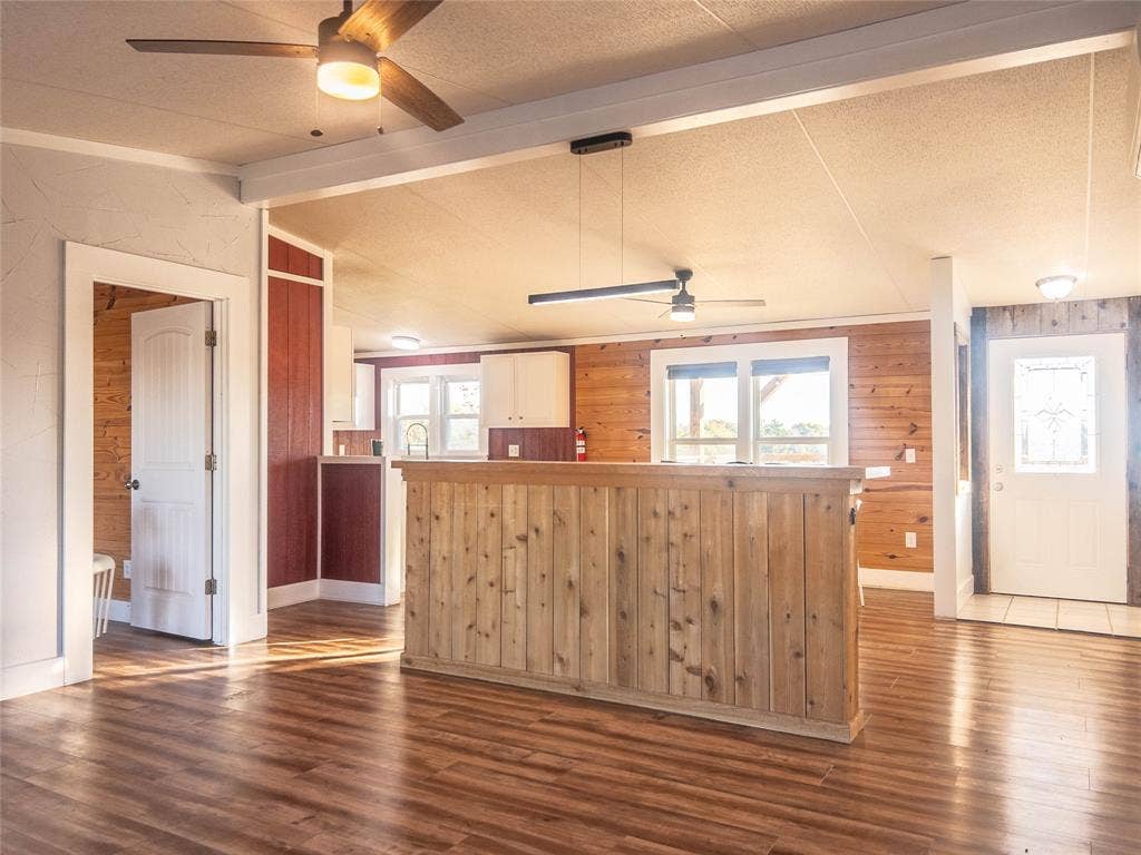 1154 Outlaw Trail, Wolfe City, TX 75496 Wood-finish flooring, wood-paneled walls, built-in wooden bar, ceiling fans, and a white six-panel door with glass insert