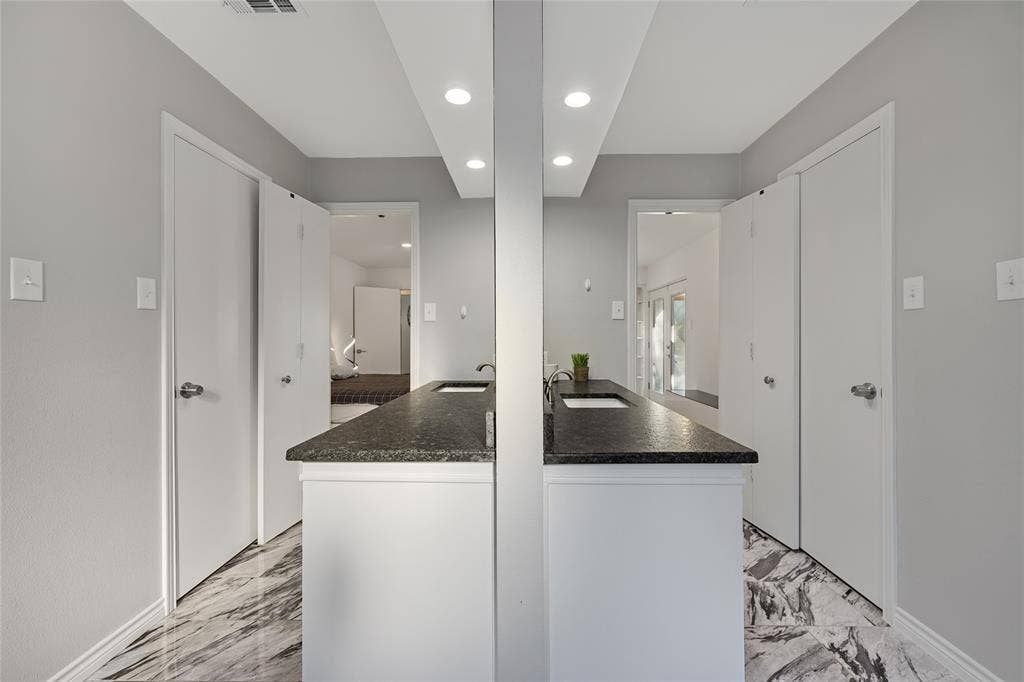 Dual vanity featuring dark stone countertops, undermount sinks, white cabinetry, recessed ceiling lighting, and patterned stone flooring