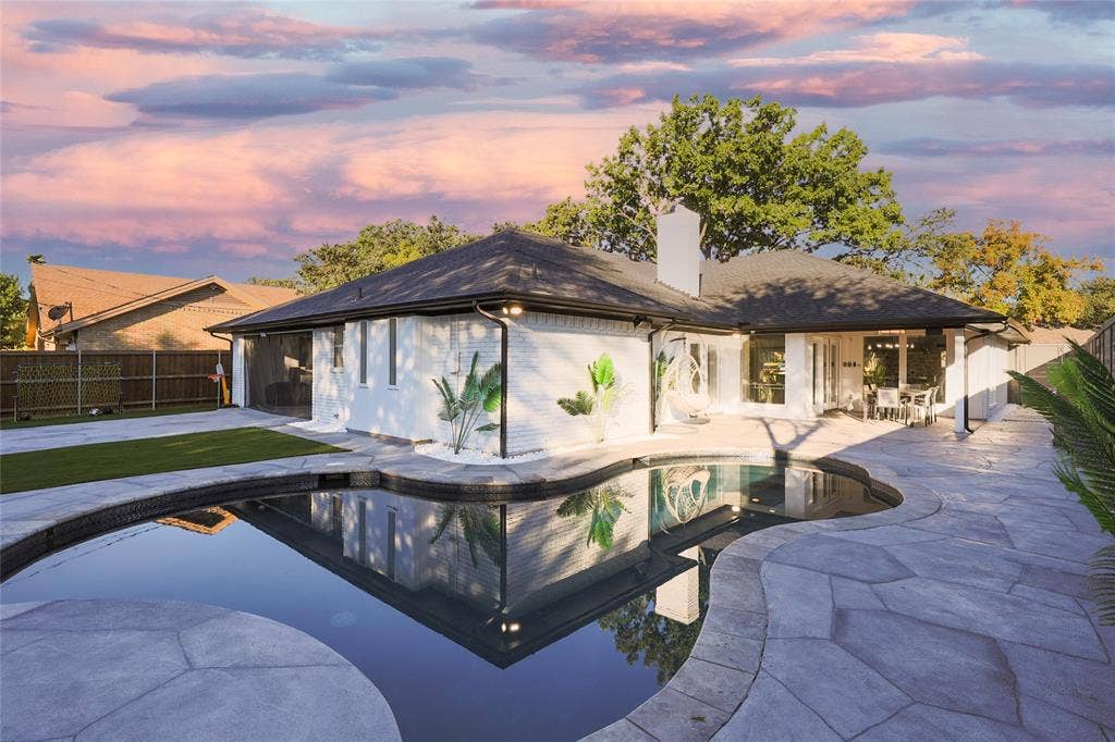 Painted brick exterior with a hipped roof, stone patio, and custom-shaped swimming pool