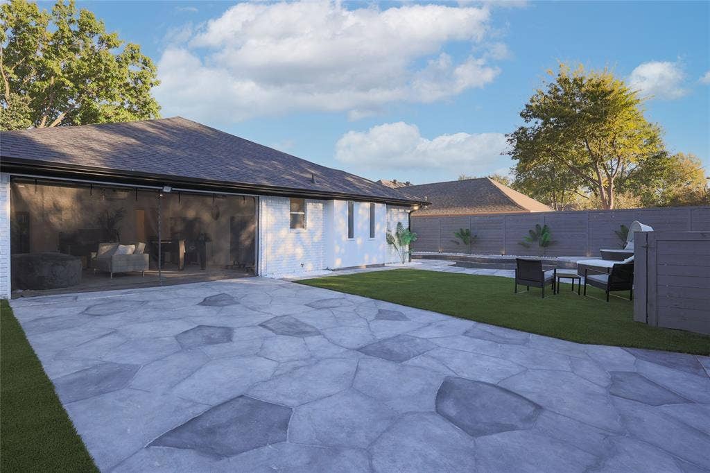 Backyard featuring a stamped concrete patio, synthetic turf lawn, white-painted brick exterior, and full-height perimeter wood fencing