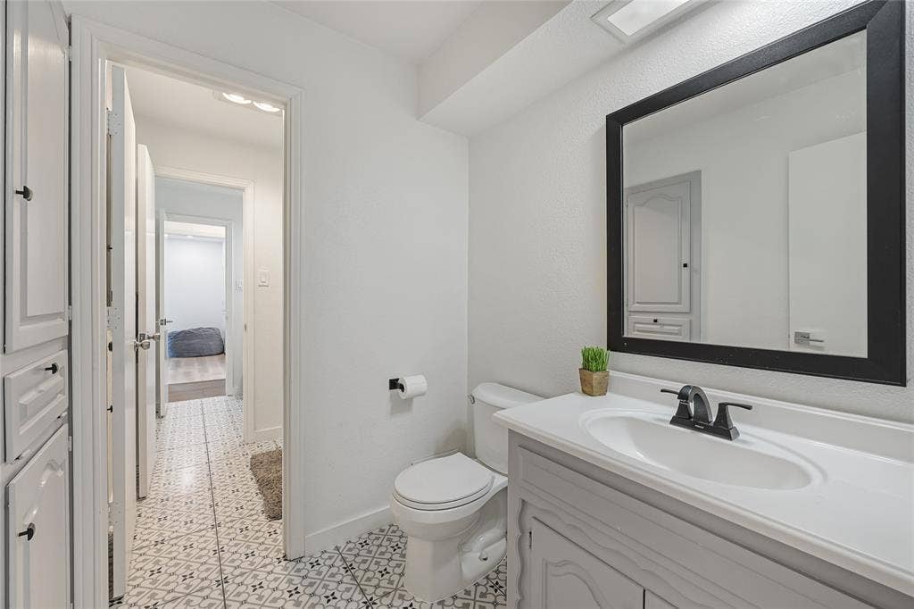 Bathroom featuring a gray vanity with an integrated basin, matte black faucet, framed mirror, and patterned tile flooring