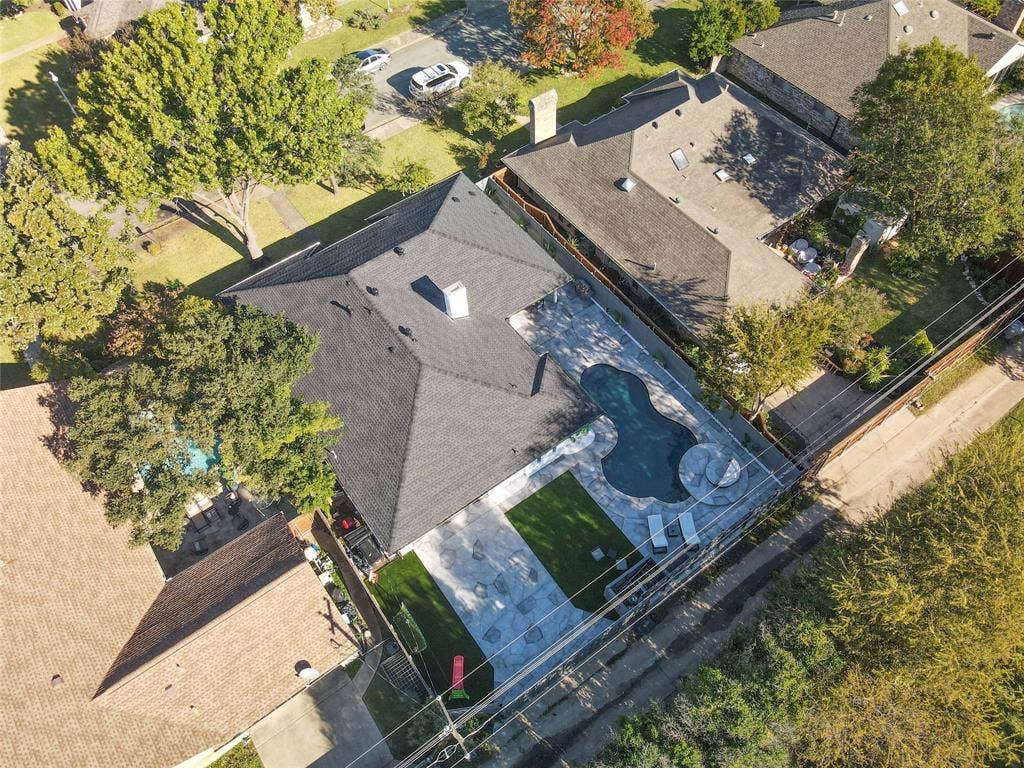 Aerial perspective of a property featuring an in-ground pool with an attached spa, expansive stone-paver hardscaping, and a maintained turf lawn