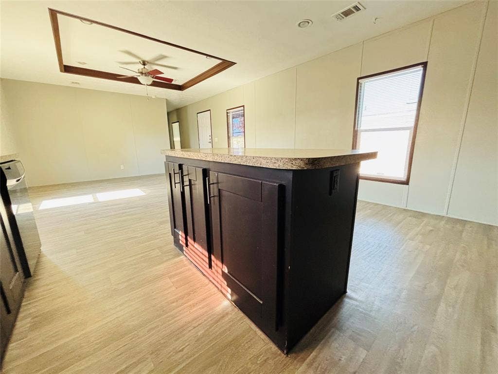 14311 Skyfrost Drive, #116, Dallas, TX 75253 Kitchen island with dark cabinetry and speckled countertop, wood-finish flooring, tray ceiling with recessed lighting, and ceiling fan