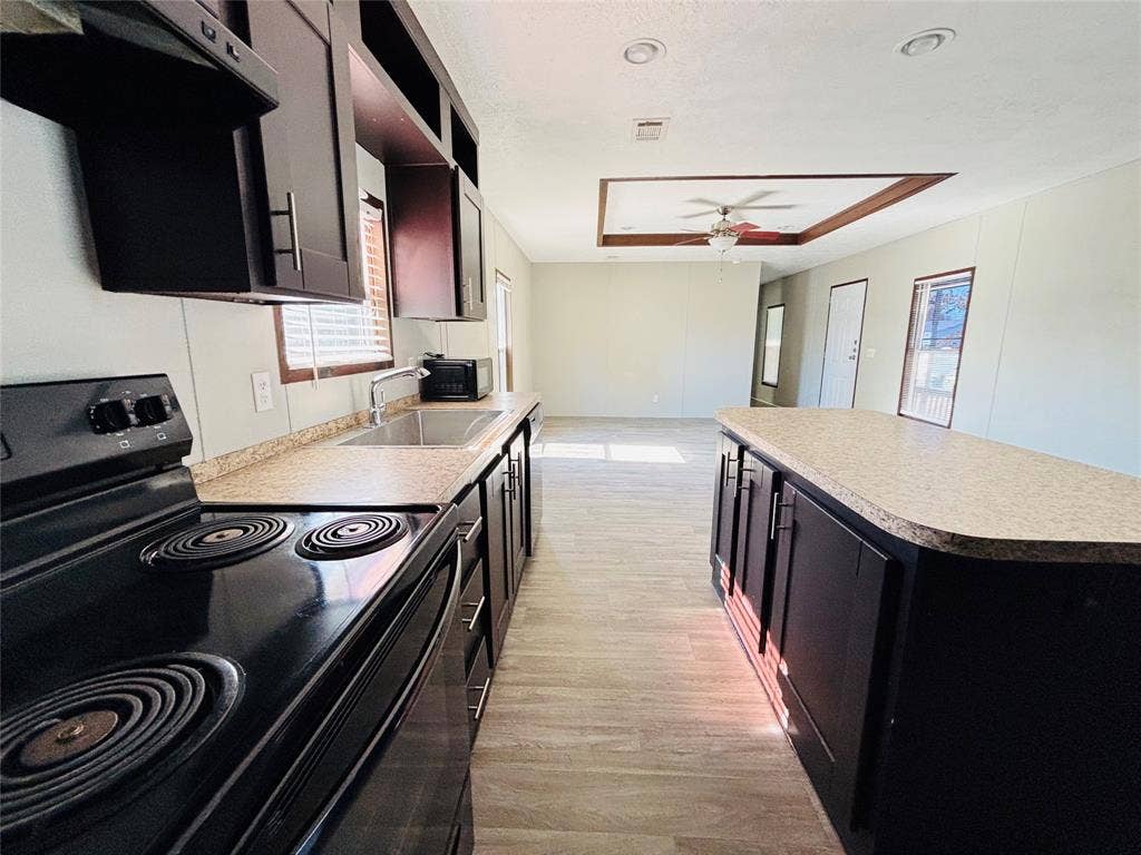 14311 Skyfrost Drive, #116, Dallas, TX 75253 Kitchen featuring dark-finish cabinetry, a central island with a solid-surface countertop, stainless steel sink with a goose-neck faucet, black electric range, and wood-finish flooring