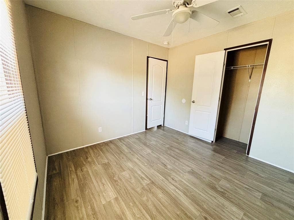 14311 Skyfrost Drive, #116, Dallas, TX 75253 Room featuring wood-finish flooring, a ceiling fan with integrated lighting, neutral wall panels, and a closet with a built-in hanging rod