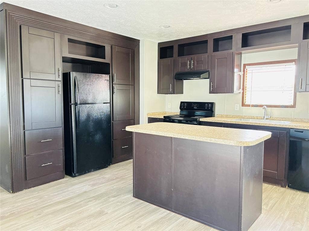 14311 Skyfrost Drive, #116, Dallas, TX 75253 Kitchen featuring floor-to-ceiling dark wood cabinetry, a central island with a solid surface countertop, wood-finish flooring, and integrated black appliances