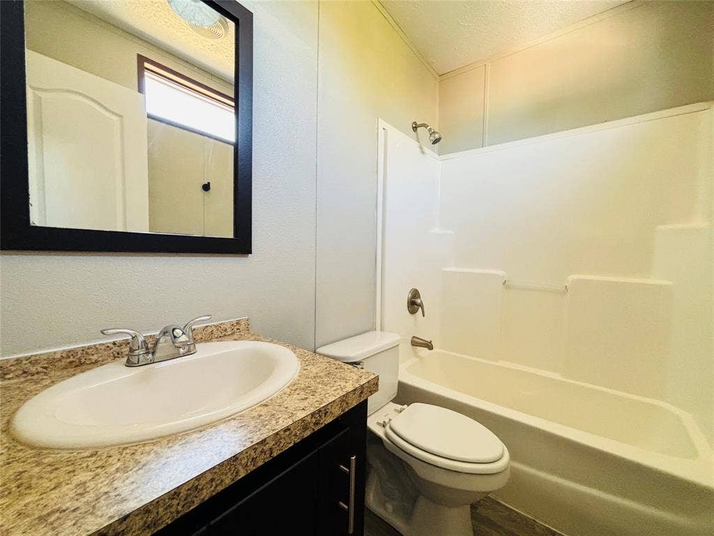 14311 Skyfrost Drive, #116, Dallas, TX 75253 Bathroom featuring a dark wood-finish vanity with a stone-patterned countertop, an integrated oval sink, a wall-mounted mirror with a black frame, and a white tub-shower surround