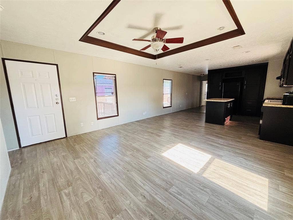 14311 Skyfrost Drive, #116, Dallas, TX 75253 Tray ceiling with dark wood-finish trim, ceiling fan, wood-finish flooring, and black cabinetry with a central kitchen island