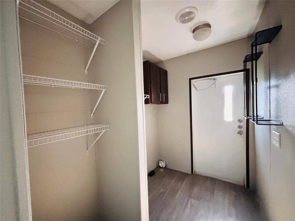 14311 Skyfrost Drive, #116, Dallas, TX 75253 Utility area featuring wood-finish flooring, white wire shelving, dark wood-tone upper cabinetry, and a flush-mount ceiling light fixture