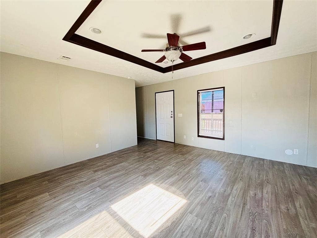 14311 Skyfrost Drive, #116, Dallas, TX 75253 Tray ceiling with dark wood-finish trim, wood-finish flooring, ceiling fan with integrated light fixture, recessed lighting, and single-panel exterior door