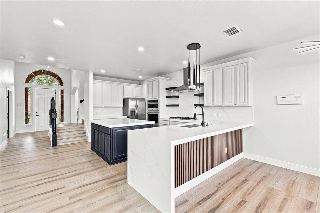 4421 Red Barn, Richardson, TX 75082 Kitchen featuring quartz countertops, wood-finish flooring, two-tone cabinetry, a fluted wood kitchen island base, and stainless steel built-in appliances