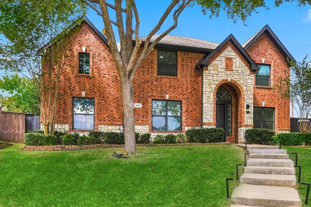 4421 Red Barn, Richardson, TX 75082 Two-story brick exterior featuring a stone-accented facade, an arched entryway, shingle roofing, and concrete front steps