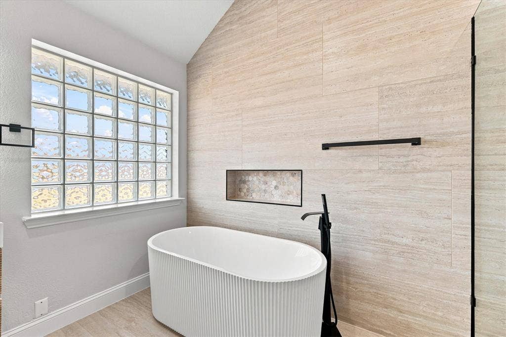 4421 Red Barn, Richardson, TX 75082 Freestanding fluted soaking tub with matte black floor-mounted faucet, floor-to-ceiling stone-finish tile wall, recessed niche, and glass block window