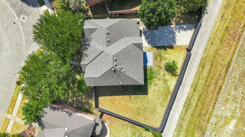 4421 Red Barn, Richardson, TX 75082 Aerial perspective featuring a multi-faceted shingle roof, concrete driveway, and a fenced backyard with mature trees