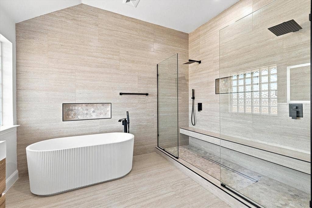 4421 Red Barn, Richardson, TX 75082 Freestanding fluted soaking tub, glass-enclosed walk-in shower with integrated bench seating, neutral linear tile walls, and matte black plumbing fixtures