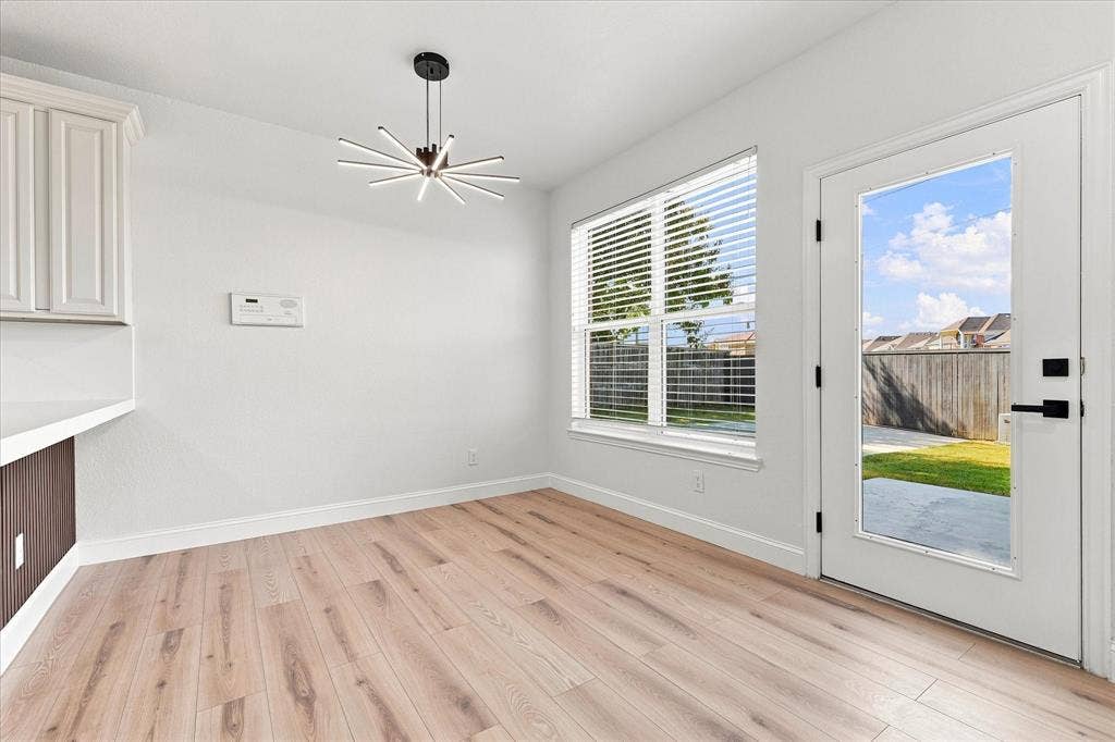 4421 Red Barn, Richardson, TX 75082 Interior space featuring wood-finish flooring, a modern multi-arm sputnik-style chandelier, horizontal window blinds, and a glass-paneled exterior door with matte black hardware