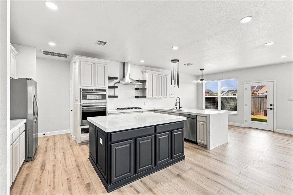 4421 Red Barn, Richardson, TX 75082 Kitchen featuring wood-finish flooring, a central island with contrasting cabinetry, stone-finish countertops, stainless steel appliances, and built-in wall ovens