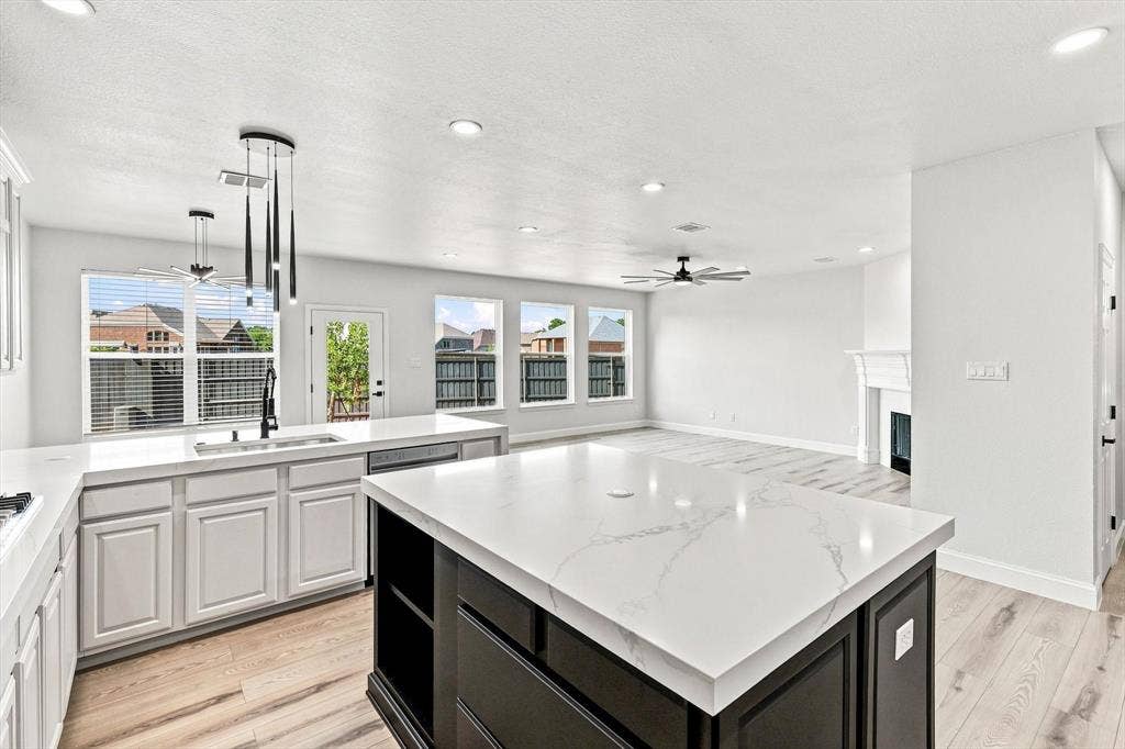 4421 Red Barn, Richardson, TX 75082 Kitchen featuring a central island with a stone-finish countertop, white cabinetry, wood-finish flooring, recessed lighting, and a fireplace with a decorative mantel