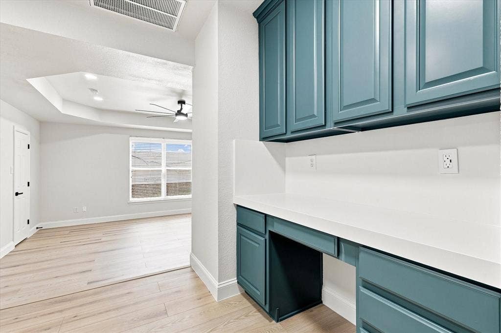 4421 Red Barn, Richardson, TX 75082 Built-in desk featuring teal cabinetry, white solid-surface countertop, wood-finish flooring, and recessed tray ceiling