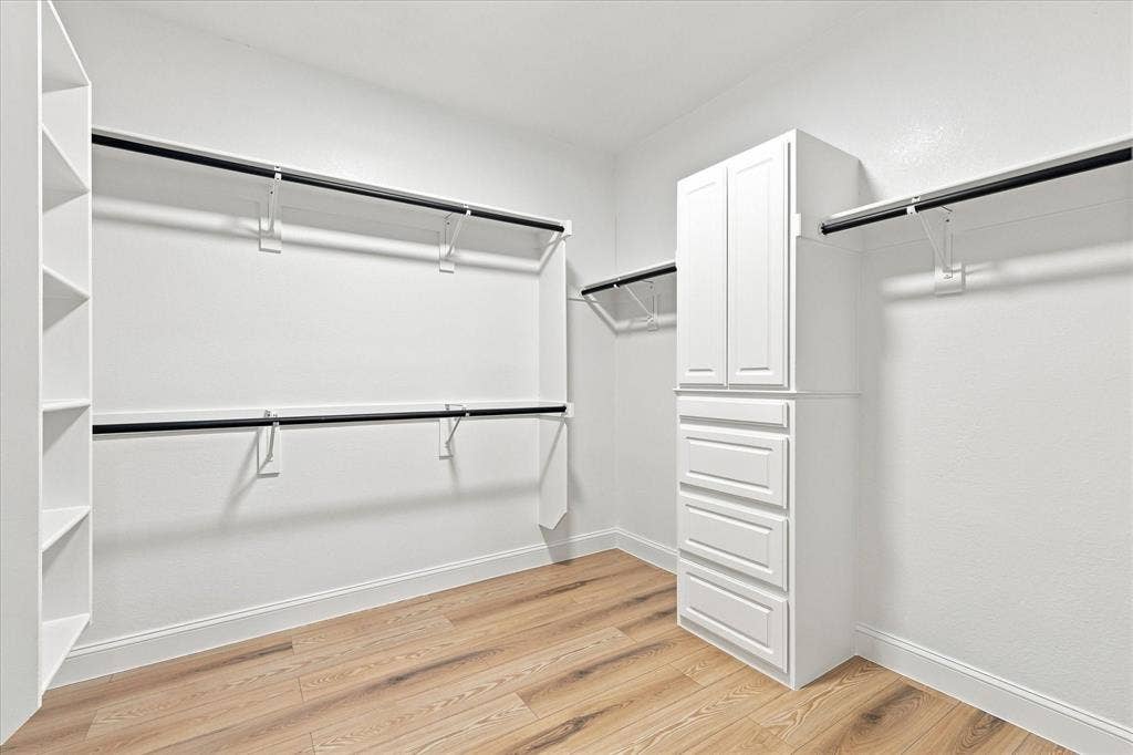 4421 Red Barn, Richardson, TX 75082 Walk-in closet featuring wood-finish flooring, built-in white cabinetry with drawers, shelving units, and double-tier hanging rods