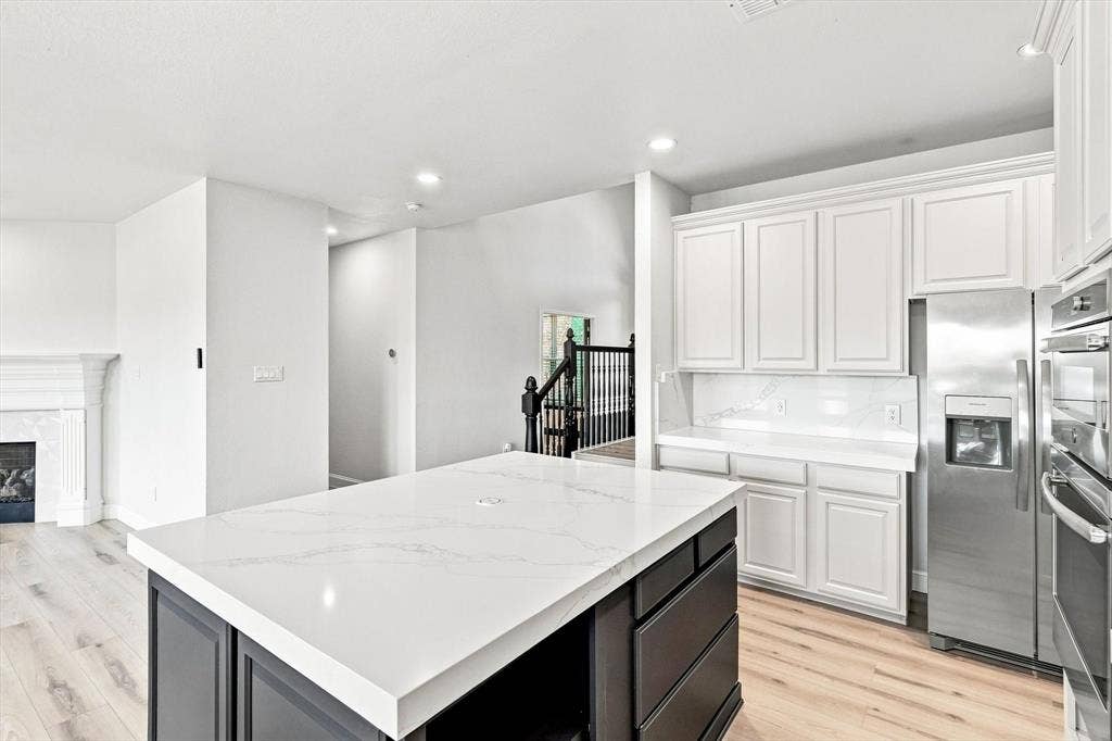 4421 Red Barn, Richardson, TX 75082 Kitchen featuring white cabinetry, an oversized central island with a contrasting dark finish and stone countertop, stainless steel appliances, and wood-finish flooring