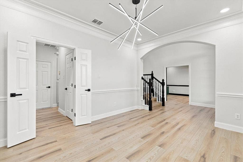 4421 Red Barn, Richardson, TX 75082 Interior space featuring wood-finish flooring, crown molding, chair rail trim, a multi-arm geometric chandelier, and an arched entry with a staircase