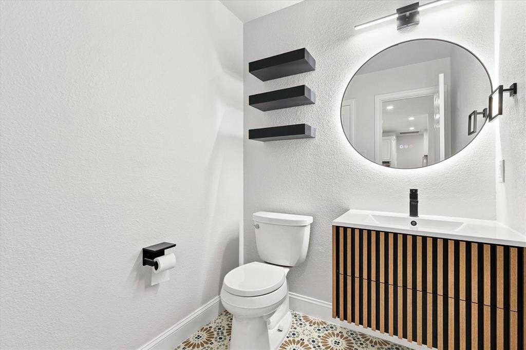 4421 Red Barn, Richardson, TX 75082 Modern vanity with vertical wood-slat detailing, white rectangular basin, matte black faucet, illuminated circular wall mirror, and patterned tile flooring