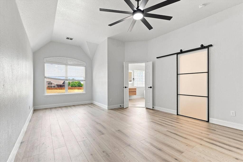 4421 Red Barn, Richardson, TX 75082 Vaulted ceilings, wood-finish flooring, multi-pane window with arched transom, matte black ceiling fan, and sliding barn door with frosted glass panels