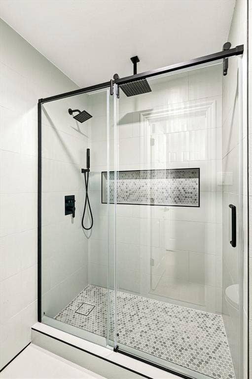 4421 Red Barn, Richardson, TX 75082 Walk-in shower featuring a frameless glass sliding door with matte black hardware, rainfall showerhead, adjustable handheld shower wand, and a built-in recessed tiled niche with hexagonal mosaic tile accents