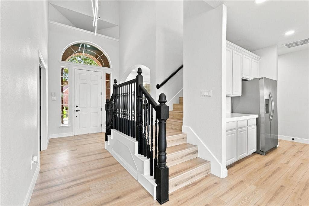 4421 Red Barn, Richardson, TX 75082 High-ceilinged entry featuring a white arched-top front door with sidelights, wood-finish flooring, and a staircase with black-painted wood balusters and handrails