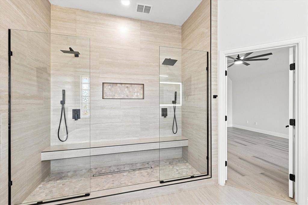 4421 Red Barn, Richardson, TX 75082 Walk-in shower featuring floor-to-ceiling tile, a built-in stone bench, dual rainfall shower heads with hand-held sprayers, a linear drain, and frameless glass enclosure
