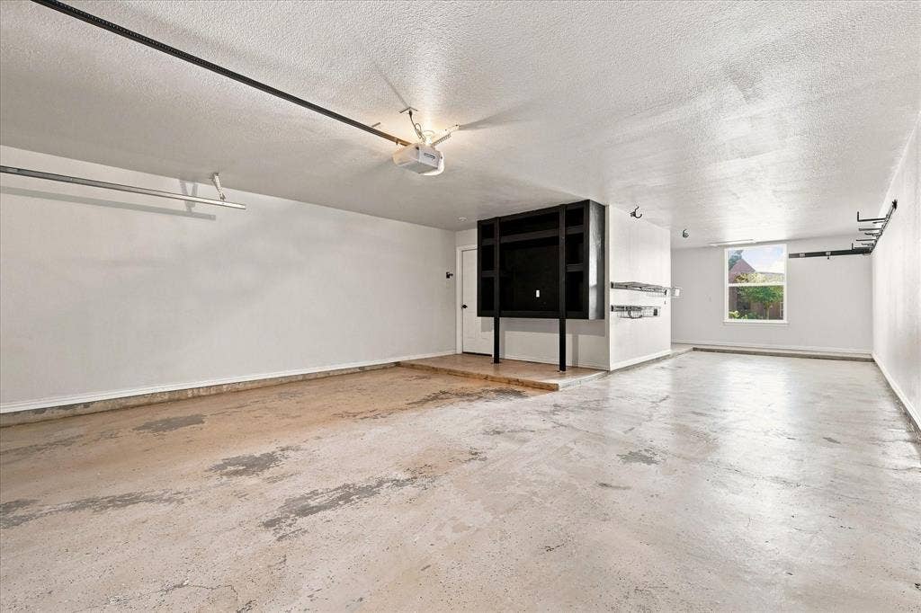4421 Red Barn, Richardson, TX 75082 Multi-car garage featuring concrete flooring, built-in black cabinetry, overhead storage racks, and a single-pane window