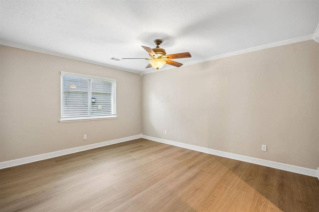 1213 Lombardy Drive, Plano, TX 75023 Warm wood-look flooring complements the soft neutral palette in this welcoming bedroom, while white baseboards and window trim add a polished finishing touch. Natural light filters through the window blinds, and the ceiling fan provides added comfort. The expansive wall space offers flexibility for a variety of bedroom layouts and design styles.