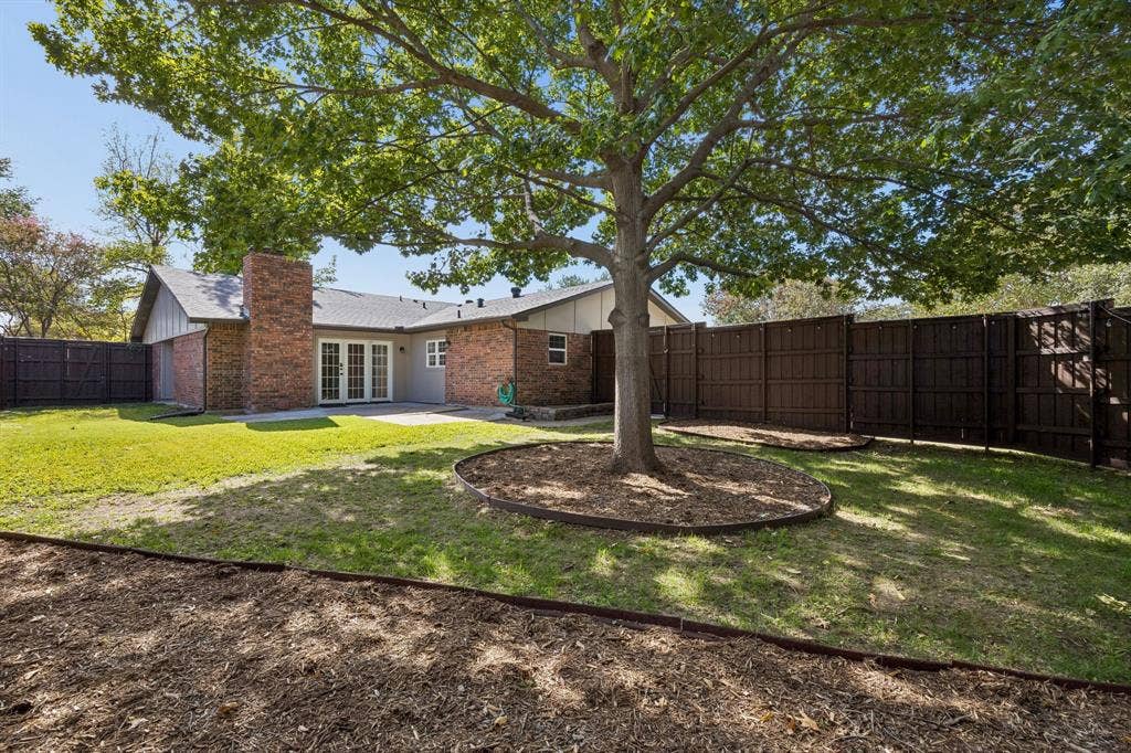 1213 Lombardy Drive, Plano, TX 75023 A mature shade tree serves as the centerpiece of this inviting backyard, offering natural beauty and a welcome retreat from the Texas sunshine. The fenced yard provides privacy, while the combination of grassy areas and landscaped mulch beds creates opportunities for outdoor enjoyment, gardening, or additional landscaping enhancements.