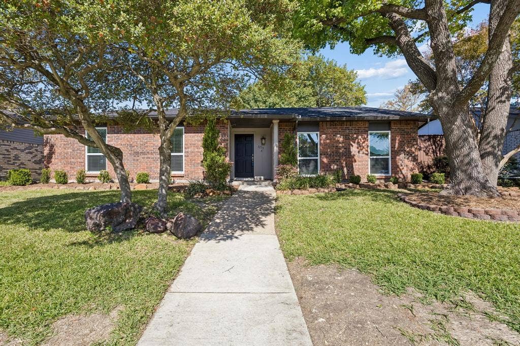 1213 Lombardy Drive, Plano, TX 75023 A charming brick exterior welcomes you with timeless appeal, mature shade trees, and beautifully established landscaping. A welcoming walkway leads to the covered front entry, while the manicured lawn, natural stone accents, and classic architectural details create an inviting first impression.