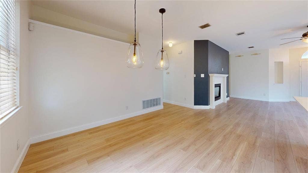 10514 Greenbriar Lane, Rowlett, TX 75089 Light-filled interior featuring wood-finish flooring, two glass pendant light fixtures, a fireplace with a decorative mantel, and a neutral color palette